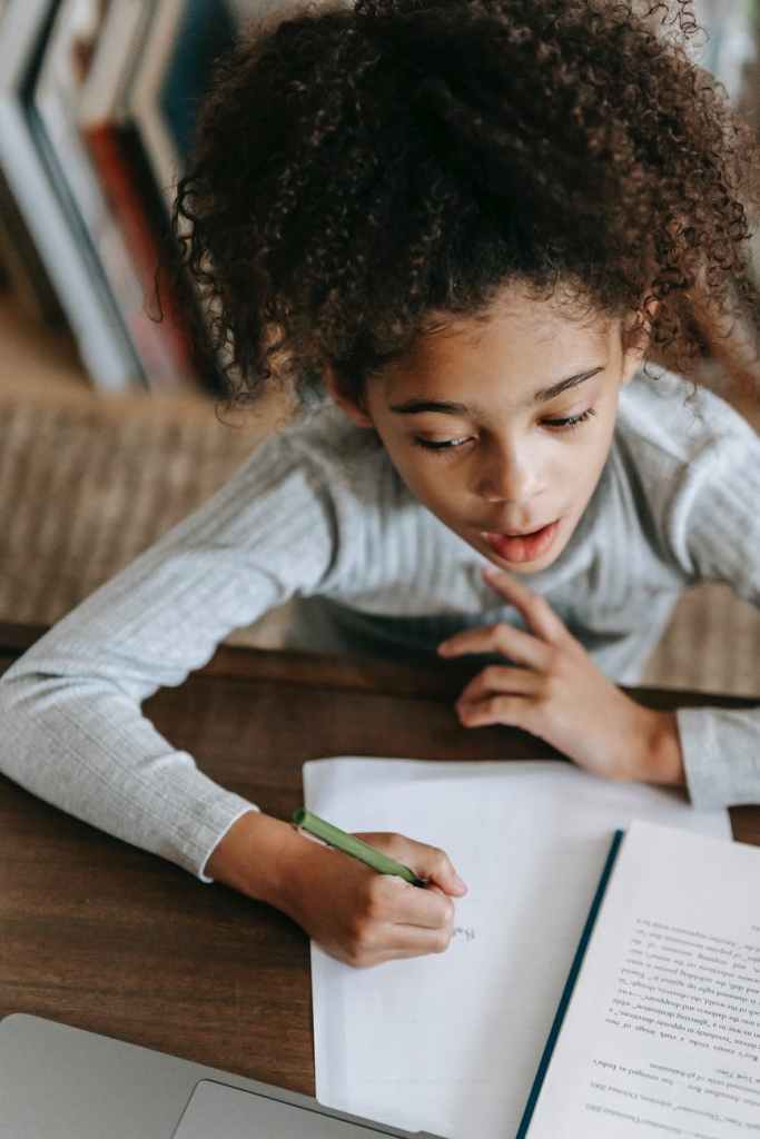 a little girl thinking and writing on a piece of paper.