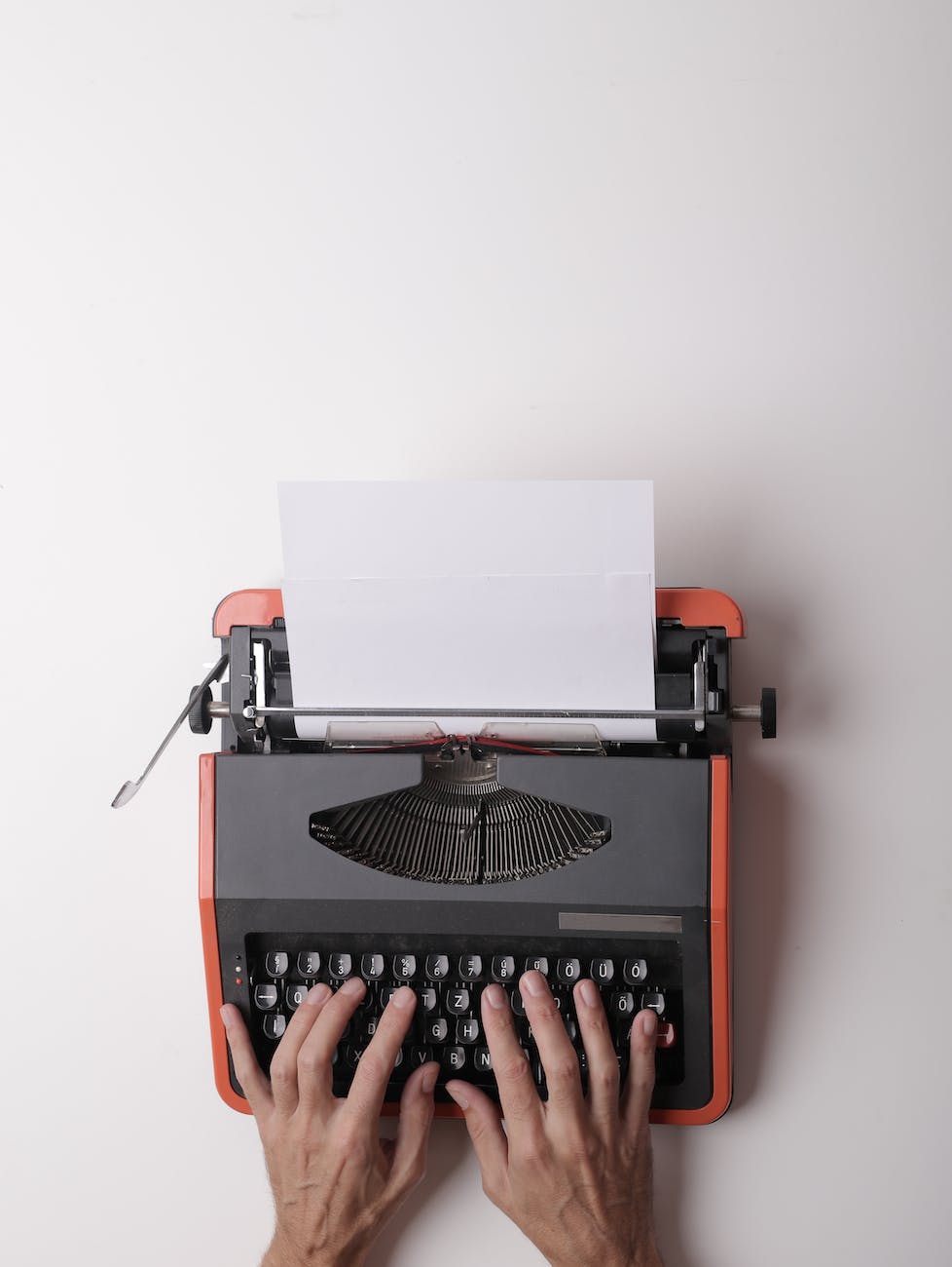 hands typing on an orange and black typewriter.